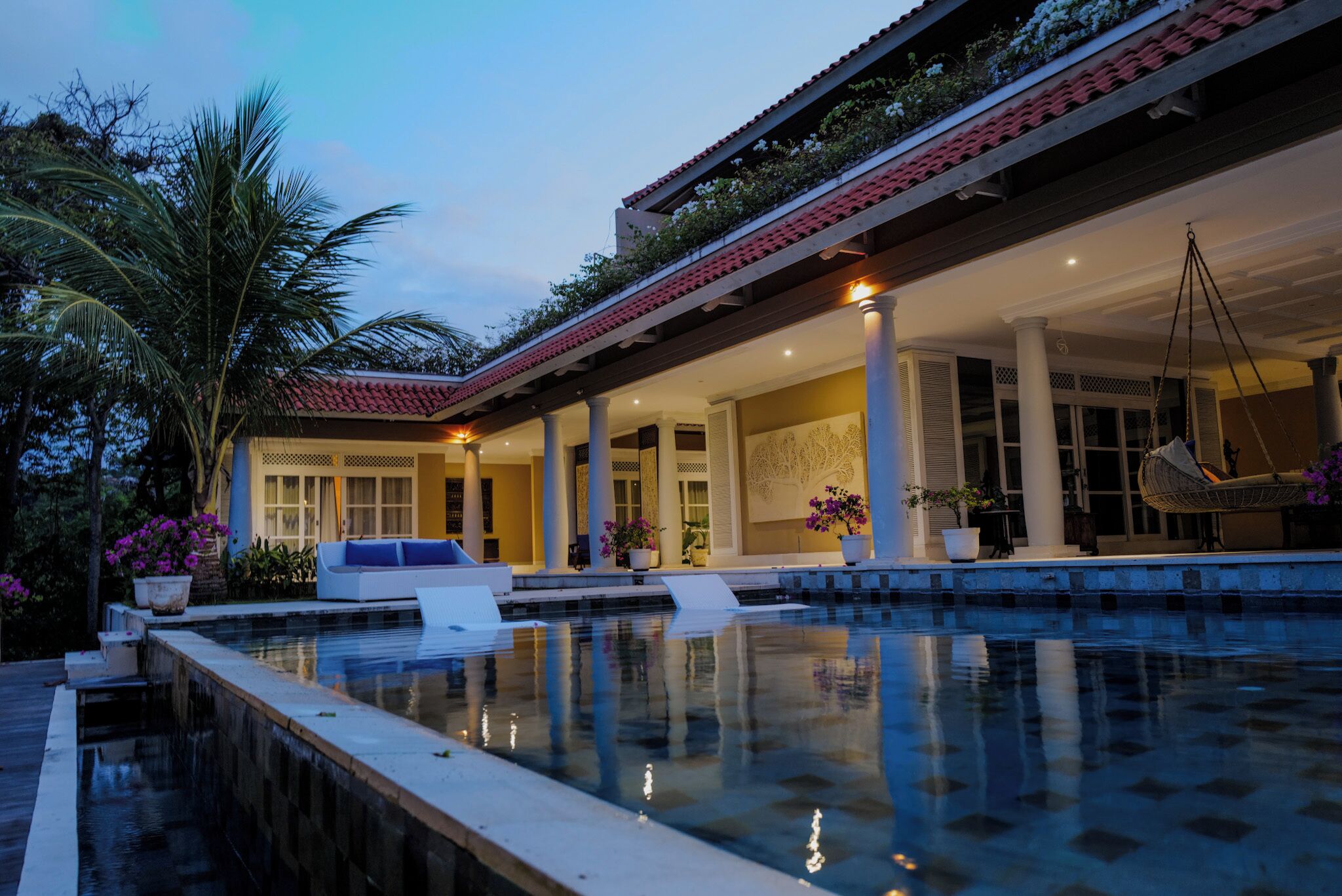 Zona de piscina con un espacio de descanso cubierto, columnas y una silla colgante.