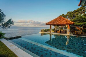 An infinity pool with a clear view of the sea, a gazebo with outdoor seating, and a well-maintained lawn. - Raaga Samudra Villa (Padangbai)