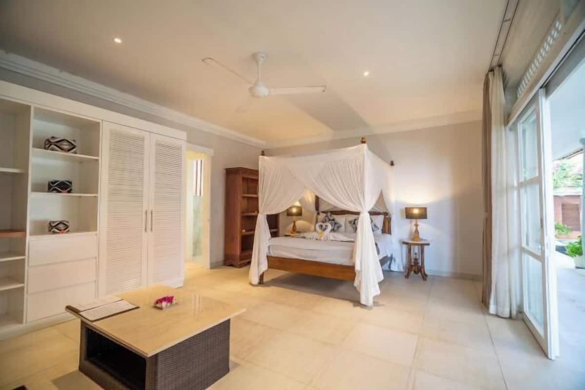 A bedroom with a canopy bed, a wardrobe, a bedside table, and a window.
