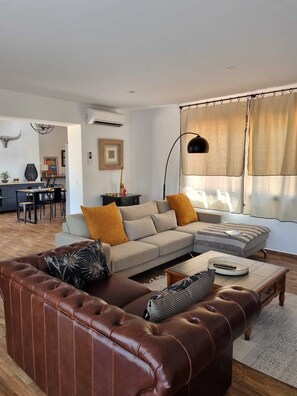 A modern living room with a leather sofa, a dining area with a table and chairs, and a large window with curtains. - VILLA SOUS LE PIN - 2 BDRMS - SWIMMING POOL (Zonza)