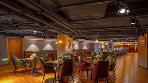 Un restaurant doté d’un plancher en bois, de chaises recouvertes d’un tissu vert et marron, et d’un éclairage suspendu.