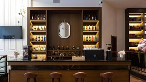Un coin bar avec des étagères en bois où sont exposées des bouteilles, un ordinateur portable et trois tabourets.