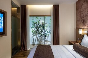 Hotelkamer met een bed, een houten nachtkastje, een globe bevestigd aan de muur, en een decoratieve plant in het midden.