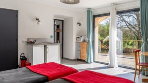 Habitación de hotel moderna con dos camas, kitchenette, comedor y balcón con vistas.