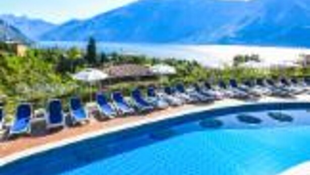 A poolside area with lounge chairs and a view of mountains and a lake. - Residence Oasi Bilo 1 2 Pax (Limone sul Garda)