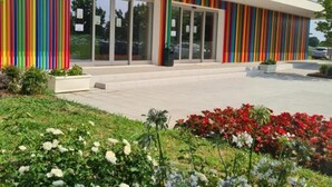 A modern building with a colorful striped facade, large glass doors, and a well-maintained garden with various flowers. - Residence Eden Bilo 4 HB (Castelnuovo del Garda)