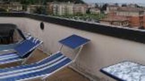 Terraza en la azotea con sillones de descanso y vistas a una colina y edificios.