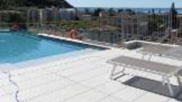 Zona de piscina con sillones de descanso y vista al mar.