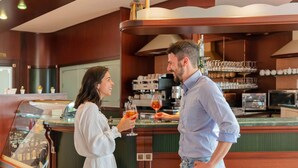 A bar area with a counter, a coffee machine, and shelves with glasses and cups. - Residence Nettuno Bilo (Peschiera del Garda)
