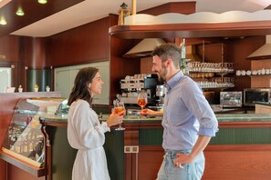 A bar area with a counter, a coffee machine, and shelves with glasses and cups. - Residence Nettuno Bilo (Peschiera del Garda)