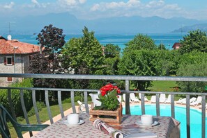 A balcony with a table, chairs, and a view of a swimming pool and mountains. - Residence Nettuno Bilo (Peschiera del Garda)