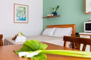 A hotel room with a bed, a desk, a chair, a TV, a framed picture on the wall, and a plant on a shelf. - Residence Nettuno Bilo (Peschiera del Garda)