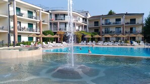 A hotel with a swimming pool, lounge chairs, and a fountain. - Residence Nettuno Bilo (Peschiera del Garda)