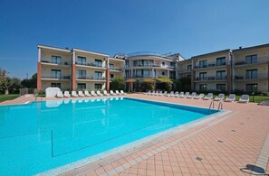A swimming pool with lounge chairs, a multi-story building with balconies, and a clear sky. - Residence Nettuno Bilo (Peschiera del Garda)
