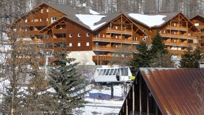 A multi-story wooden lodge with balconies, surrounded by snow-covered trees and a mountainous backdrop. - Les Chalets du Verdon 2p5n (Allos)