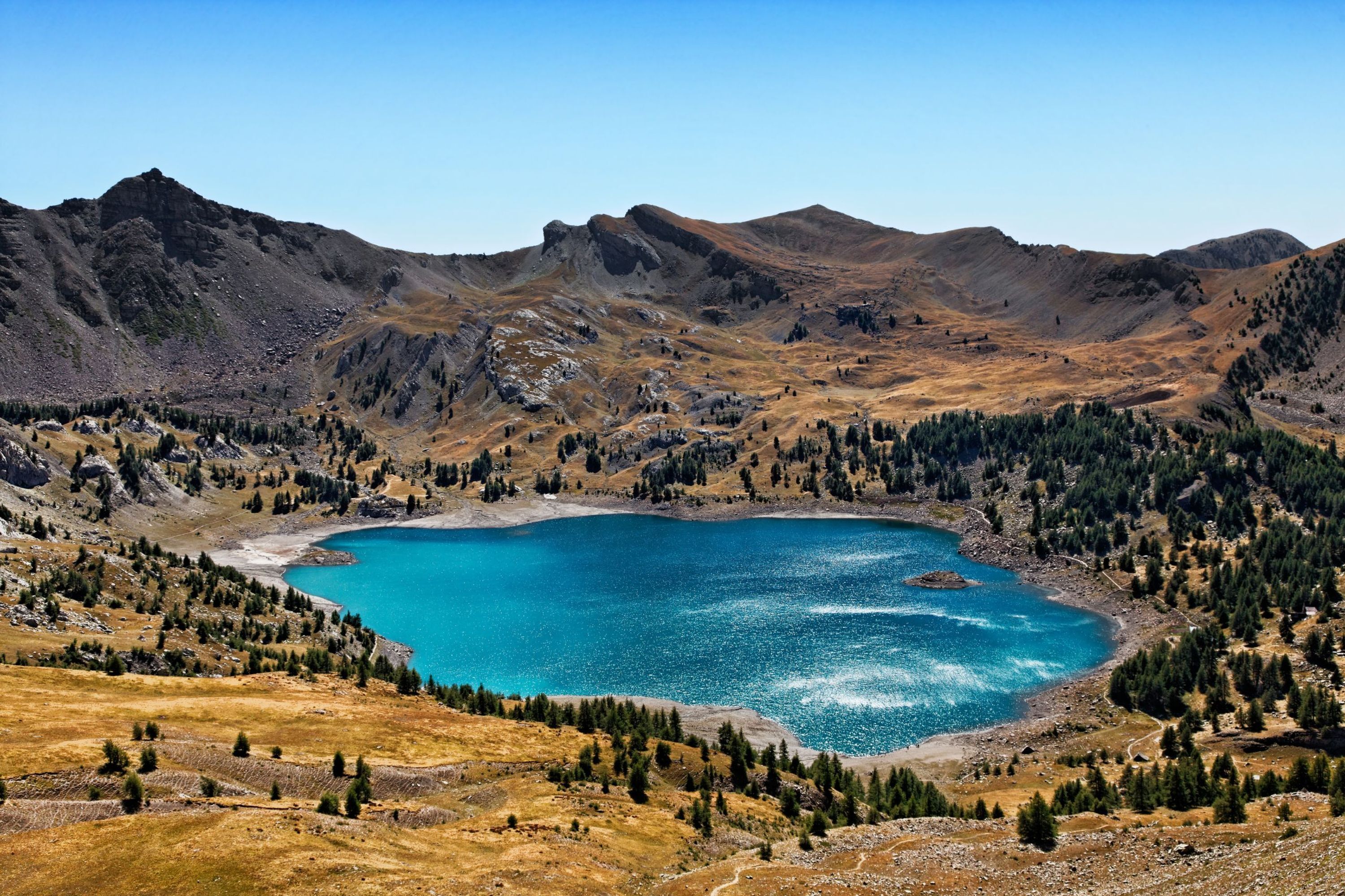 Un paysage montagneux avec un lac entouré de zones boisées et de terrains rocheux.