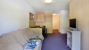 A compact living space with a sofa, a small table, a television on a stand, and a kitchenette in the background. - Les Chalets du Verdon 2p5n (Allos)