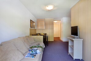 A compact living space with a sofa, a small table, a television on a stand, and a kitchenette in the background. - Les Chalets du Verdon 2p5n (Allos)