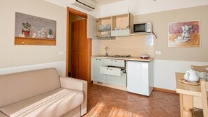 A compact kitchen with a microwave, stove, and cabinets, adjacent to a living area with a sofa and a dining table. - Residence Eden Bilo 4 BB (Castelnuovo del Garda)