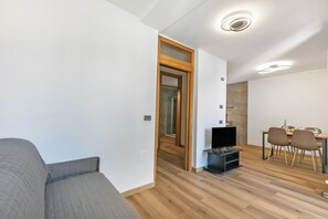 A modern living room with a grey sofa, wooden flooring, a dining area with a table and chairs, and a TV stand. - Residenza I 3 Mori B (Arco)
