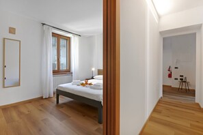 A modern bedroom with a wooden floor, a bed with white linens, a window with curtains, and a bedside table with a lamp. - Residenza I 3 Mori B (Arco)