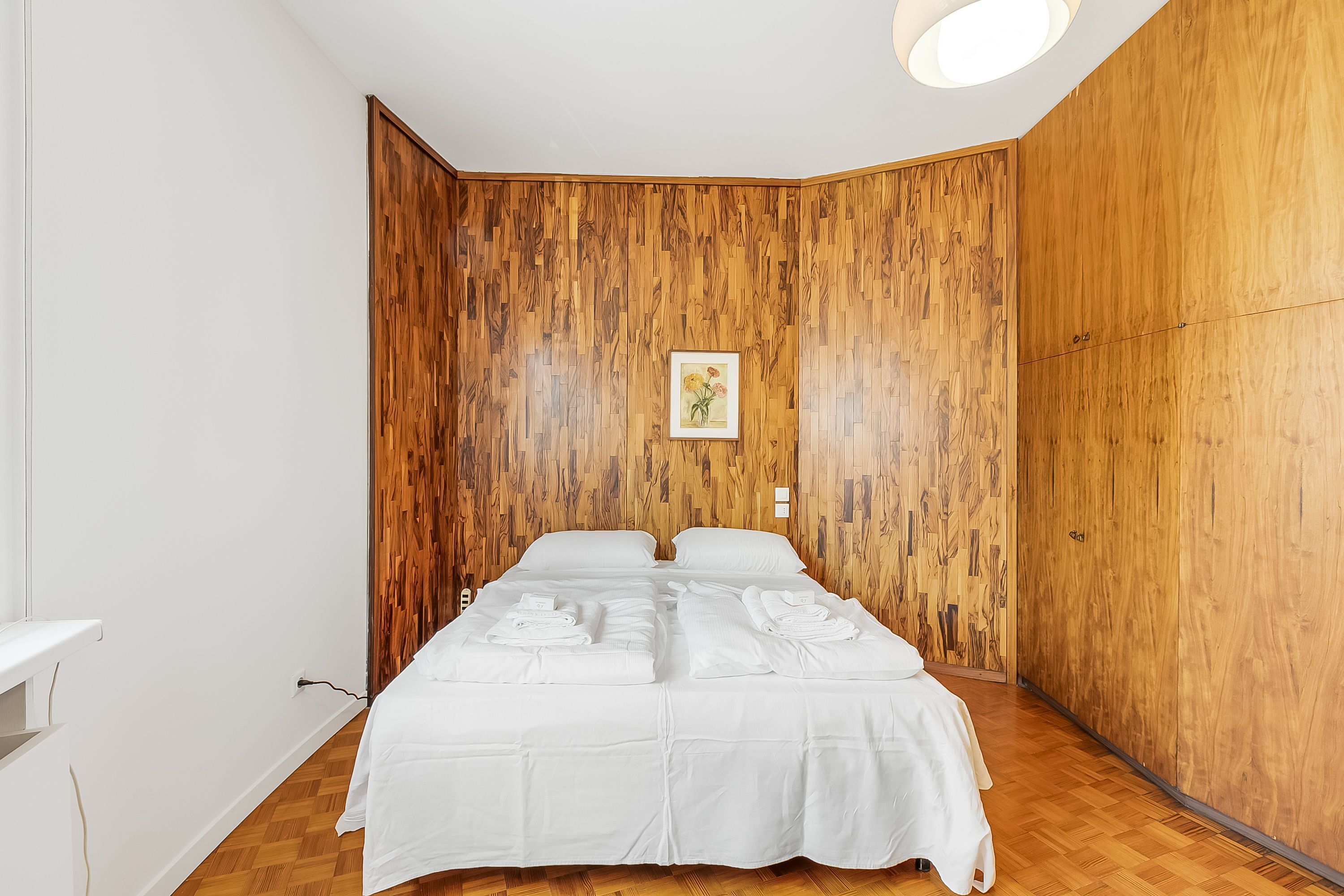 A bedroom with a wooden panel wall, a bed with white linens, and a small framed picture on the wall.