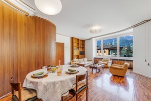 A modern living room with a dining area, wooden paneling, a large window with a mountain view, and a cozy seating arrangement. - The Arco Round House (Arco)
