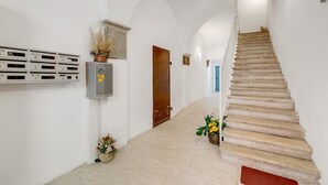 A hallway with a wooden staircase, white walls, and a door.
