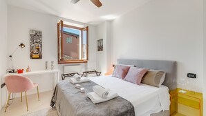 A modern bedroom with a bed, bedside table, desk, chair, and artwork.