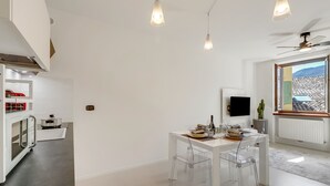 A modern kitchen with a built-in oven, a dining area with a white table and clear chairs, and a ceiling fan.