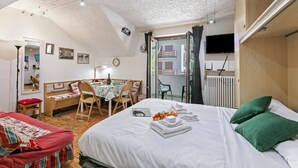 Ein Schlafzimmer mit einem großen Bett, einem Schreibtisch und einem Stuhl. An der Wand befindet sich ein Fernseher und ein Fenster mit Vorhängen.