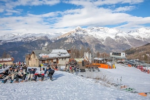 A ski resort with a chairlift, snow-covered mountains, and a building with a sign. - Appartamento La Selva Incantata (Sauze d'Oulx)