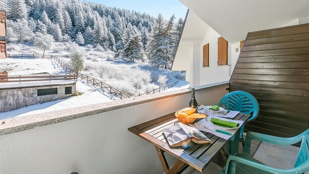Ein Balkon mit einem Holztisch, einer Flasche und einem Brot.