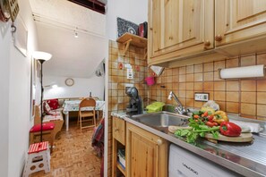 A compact kitchen with wooden cabinets, a sink, and a dining area with a table and chairs. - Appartamento La Selva Incantata (Sauze d'Oulx)
