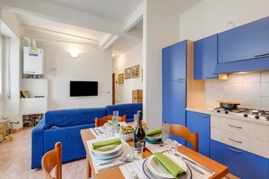 A modern kitchen with blue cabinets, a gas stove, and a dining area with a blue sofa and a wooden table set for a meal. - Seaside Binario Blu 500 M Dal Mare (Alassio)