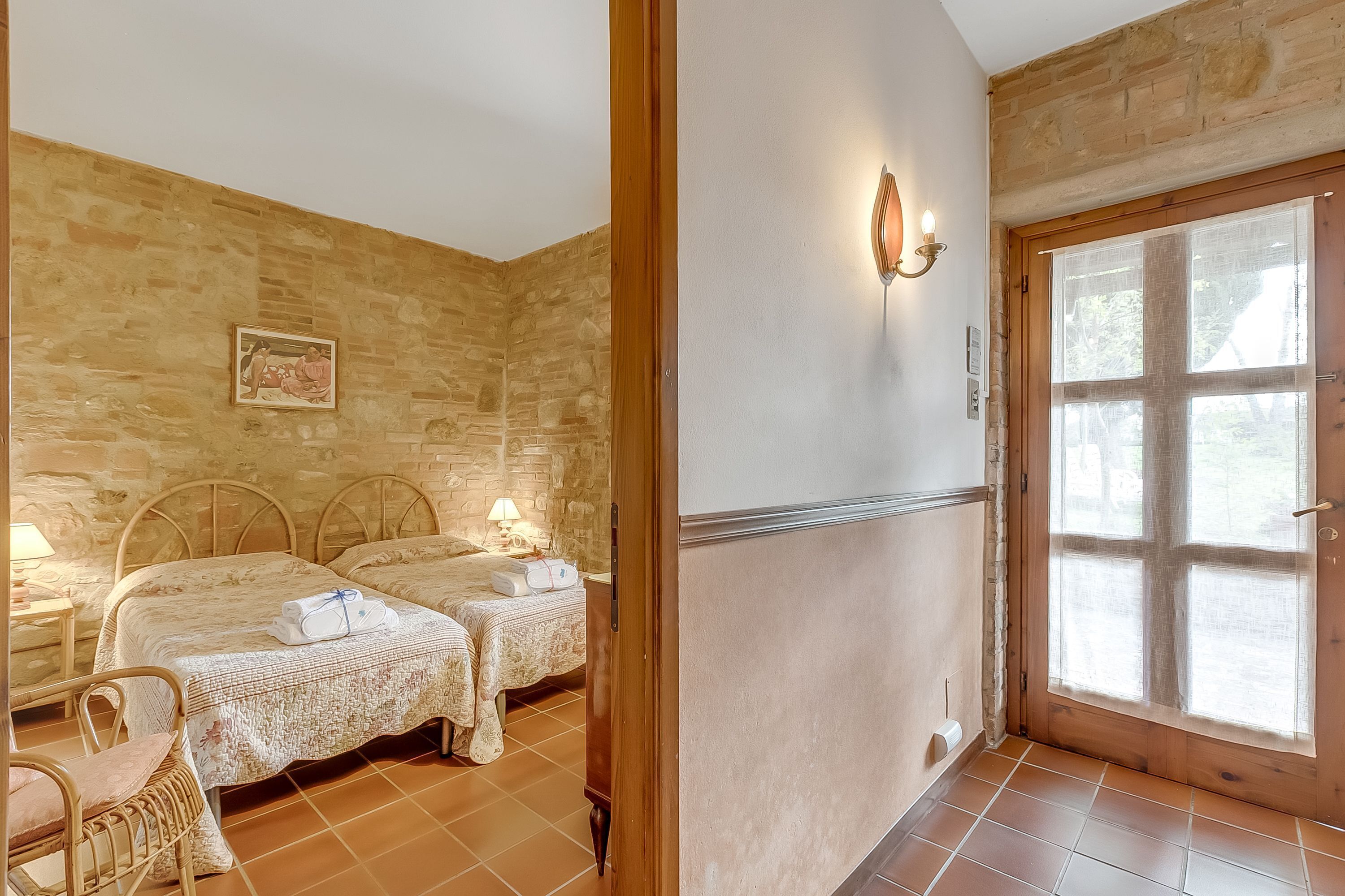 A room with two beds, a stone wall, a wooden door, and a tiled floor.