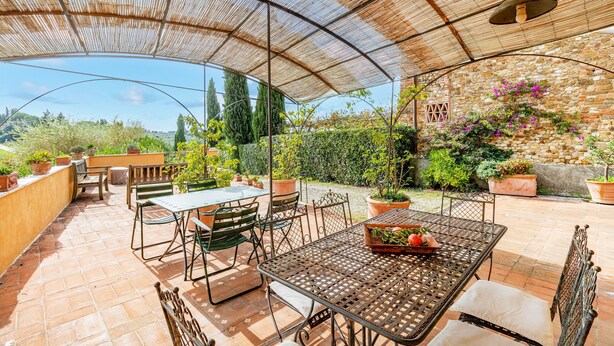 An outdoor patio with a covered seating area, a table with a fruit basket, and potted plants. - Villa Salivolpe Amazing Chianti View 14 (San Casciano in Val di Pesa)