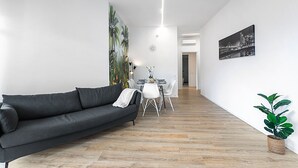 A modern living room with a dark grey sofa, a dining area with a white table and chairs, and a potted plant. - Specchio Di Cielo Arona Center (Arona)