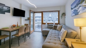 A modern living room with a sofa, dining table, chairs, a TV, and a large window with a view of a snowy landscape. - Prestige Eleven In The Center Of Town (Sestriere)