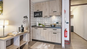 A modern kitchen with wooden cabinets, a microwave, and a sink. There is a fire extinguisher mounted on the wall and a small table with a lamp and kitchen items. - Prestige Eleven In The Center Of Town (Sestriere)