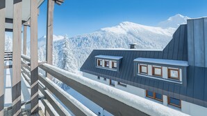 Un edificio moderno con techo inclinado y múltiples ventanas, con vistas a una cadena montañosa nevada.