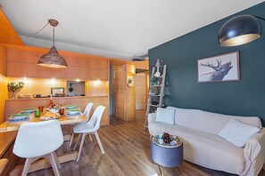 Ein modernes Wohnzimmer mit einem weißen Sofa, einem Essbereich mit Holztisch und Stühlen sowie einer Küche im Hintergrund.