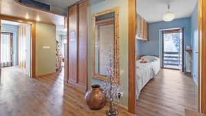 Una habitación amplia con una cama grande, piso de madera, un espejo y un jarrón con flores.