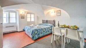 A bedroom with a bed, a dining table with chairs, a radiator, and a window. - Casa Vacanze Maimone 3 (Sanremo)