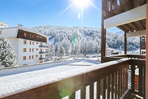 Ein Balkon mit Holzwertung, der auf eine verschneite Landschaft blickt, ein Gebäude mit mehreren Fenstern und einem strahlend blauen Himmel.