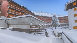 Área externa coberta de neve com um banco de madeira e uma árvore nevada.