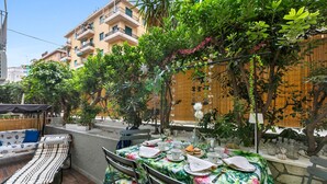 An outdoor dining area with a table set for four, surrounded by lush greenery and a wooden fence. - Casa Amorosa Town Relax Alassio (Alassio)