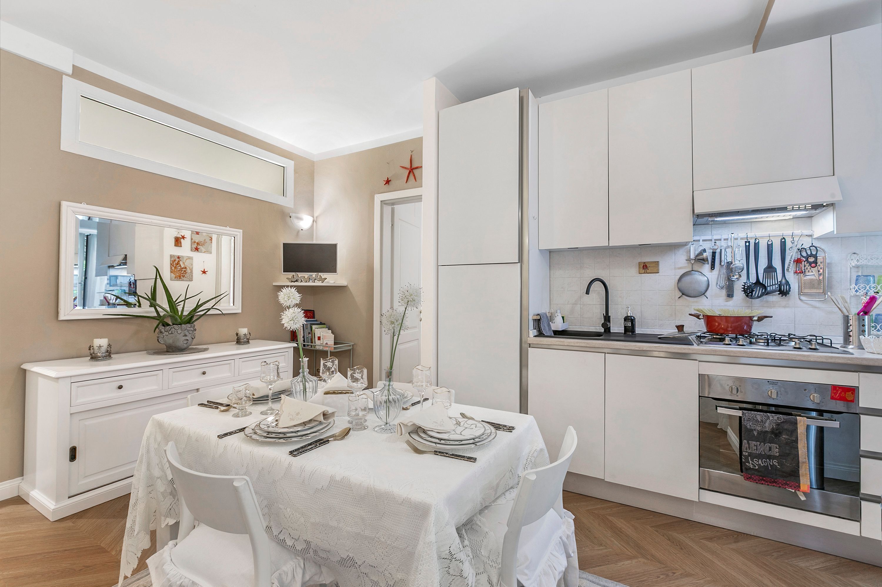 A modern kitchen with white cabinetry, a dining table set for six, and a built-in oven.