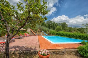 Ein Swimmingpool mit Rutsche, umgeben von roten Liegestühlen und einer Steinmauer.