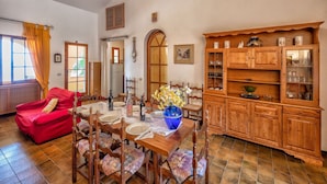 Un comedor con una mesa de madera, sillas y un sofá rojo. A la derecha, hay un armario de madera con puertas de cristal.
